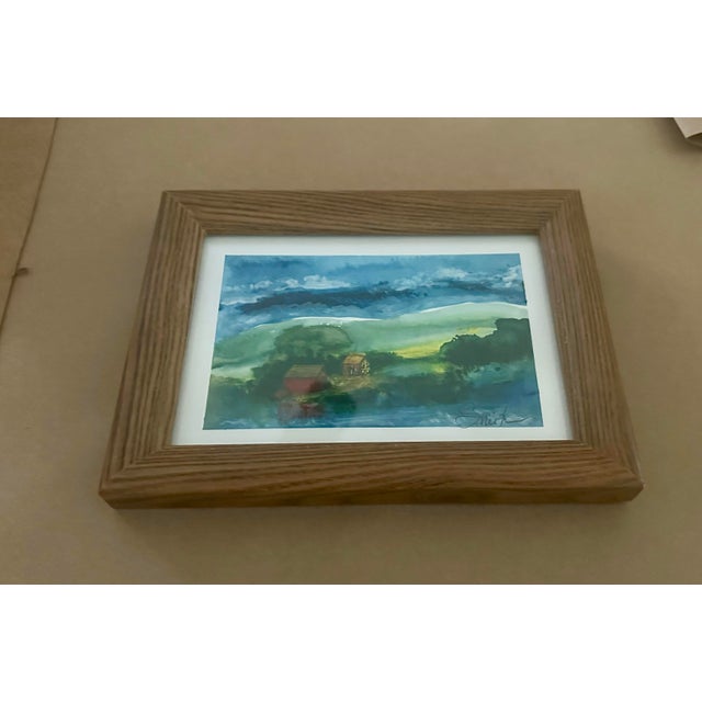 A beautifully atmospheric original watercolor landscape featuring rolling green hills, secluded country buildings, and a...