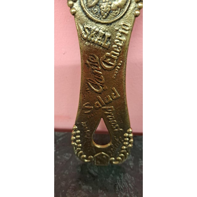 Large bronze bottle opener, featuring a top scene of two monks toasting with barrels, and the word "cheers" in various...