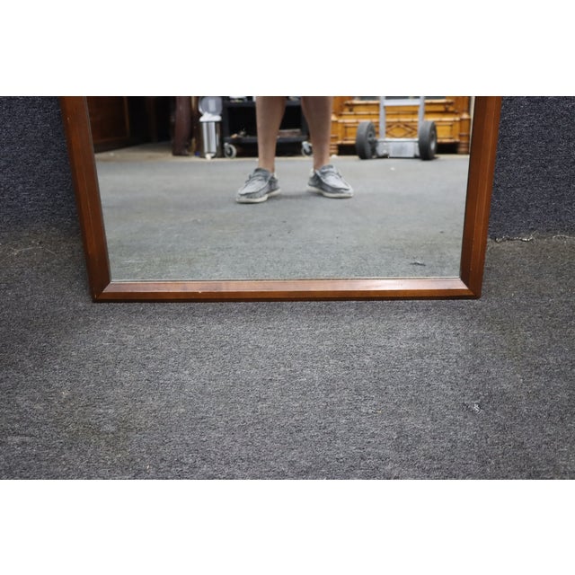 Mid-Century Modern walnut framed mirror with a clean rectangular form and stepped architectural detailing. Features a warm...