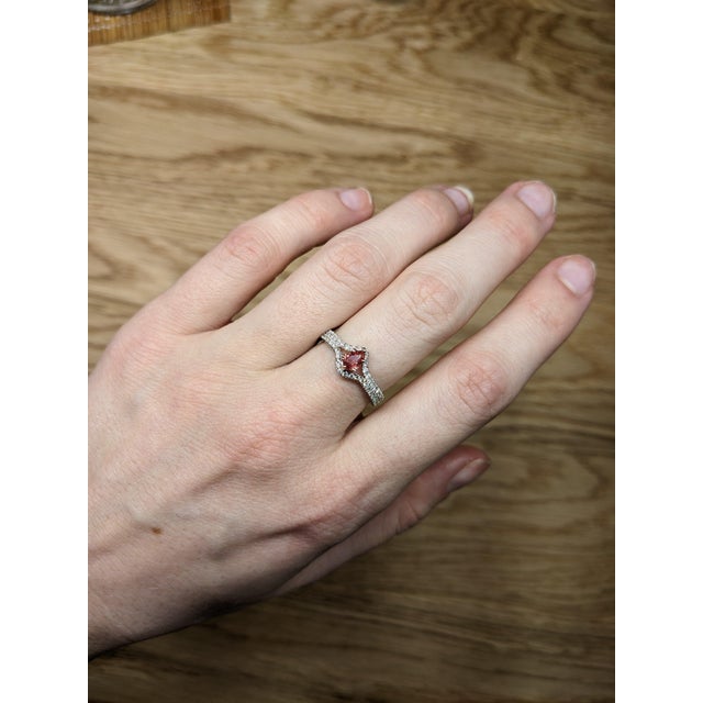 A padparadscha sapphire glows in its signature blend of pink and orange at the centre of this solid 14K white gold ring,...