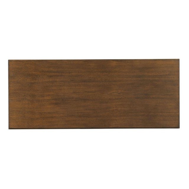 A rectangular top rests elevated above apron rails accented by brass moldings is raised on tapering KD legs.