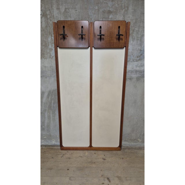 A distinctive vintage wall-mounted coat rack featuring a tall, symmetrical wooden frame with two cream-colored inset...