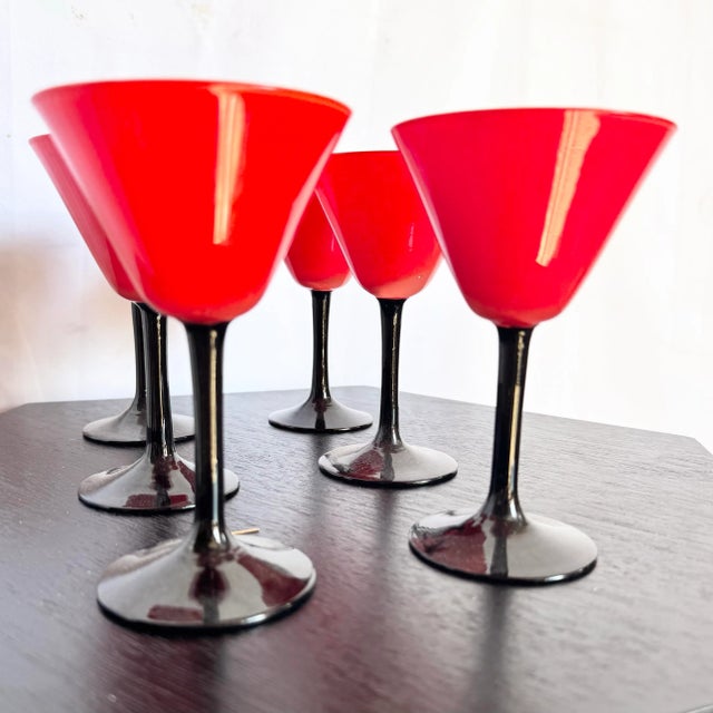 A bold and stylish set of six Art Deco-inspired cocktail glasses featuring vibrant red cups atop sleek black stems. These...