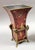 A striking decorative vase featuring a rich oxblood-red tole vessel hand-painted with butterflies, trailing vines, and...