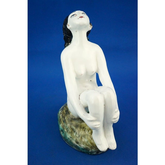 a delightful, hand-sculpted, vitrified majolica ceramic sculpture depicting a seated nude woman with her legs folded and...