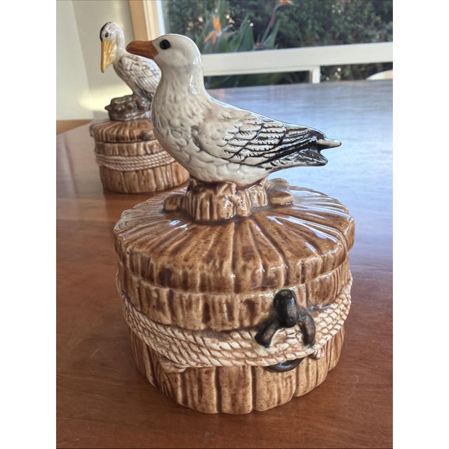 Charming vintage coastal ceramic trinket boxes featuring a pelican and seagull, each perched atop a rope-style nautical...