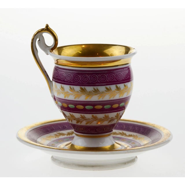 French porcelain teacup and saucer in 1830s style with alternating decorative belts of gilded branches, beads and stylized...