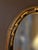Elegant vintage Federal Revival oval wall mirror featuring a dramatic black and parcel-gilt frame. Raised gold ribbon and...