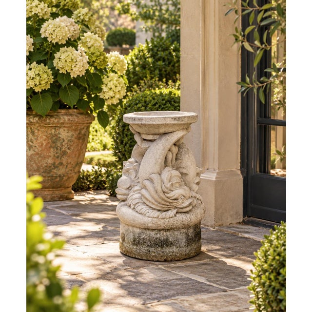 A sculptural vintage garden pedestal featuring three stylized dolphins arranged around a central support, cast in concrete...