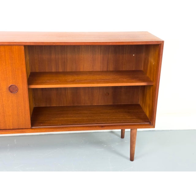 A beautifully proportioned teak sideboard with a smooth-running wooden sliding door featuring a round recessed handle....
