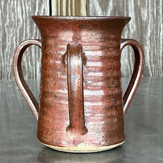 This Vintage Boho Three-Handle Studio Pottery Vase is a stunning example of artisanal craftsmanship and organic design....