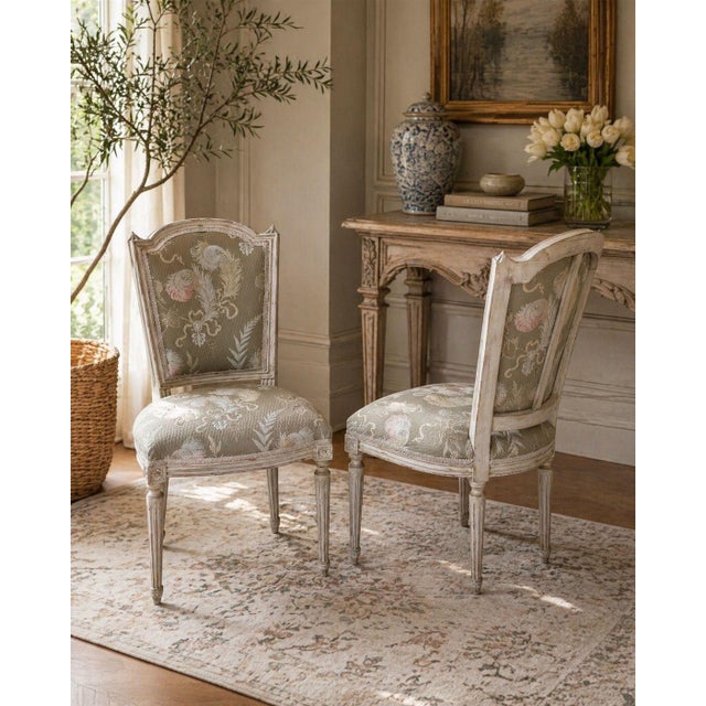 A refined pair of vintage Louis XVI style dining chairs featuring a beautifully aged painted frame and elegant, tapered...