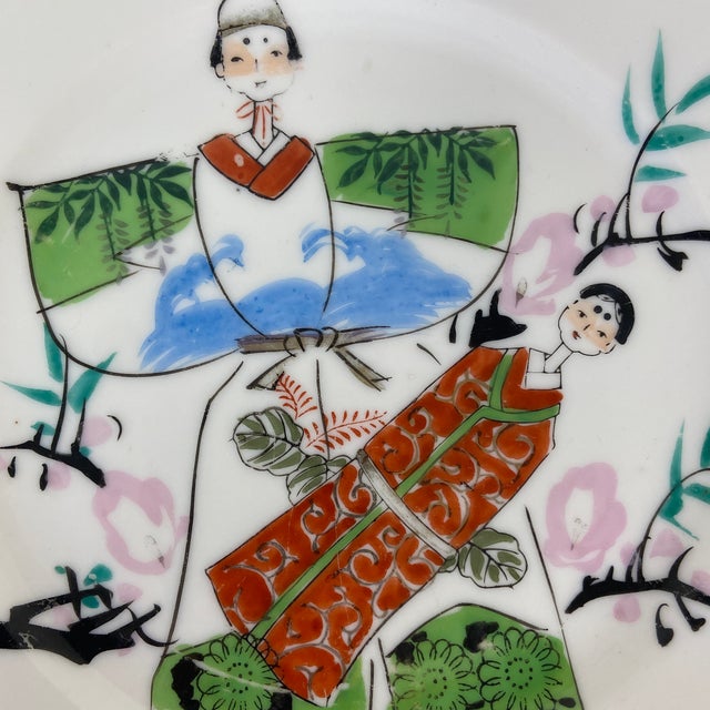 A charming unique mid-century Japanese porcelain plate featuring two kimono-clad court figures rendered in a traditional...