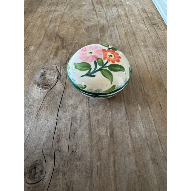 A charming miniature ceramic covered dish featuring a hand-painted floral motif in soft pink and coral tones with green...