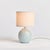 With a petite ceramic body and a soothing sage glaze, this lamp adds warmth to any setting. Topped off with a natural...