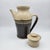 Hand-thrown stoneware lidded pitcher with speckled cream upper glaze, dark brown lower half, and a textured transitional...