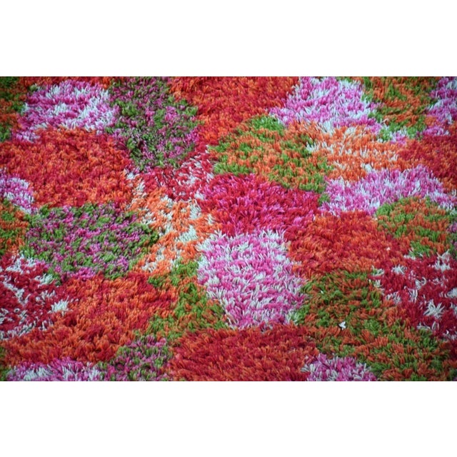 A large mid century modern shag style rug rich in pink red and green blends. Chairs used to show size of rug. Chairs not...