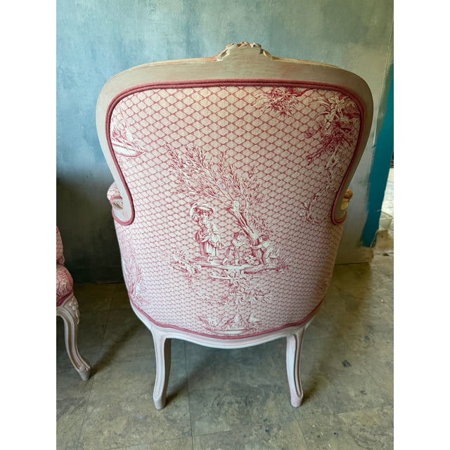 Lovely pair of 20th century French bergere chairs. Upholstered in a pinky red Toile De Jouy fabric with down cushions.