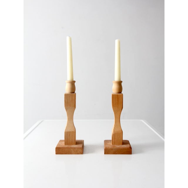 Pair of handmade wooden candlesticks with faceted stems, square bases, and a natural wood finish. Their clean sculptural...