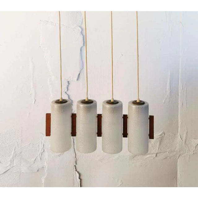 This ceiling lamp made of glass and rosewood elements is decorated in a clear mid-century style and dates from the 1960s....