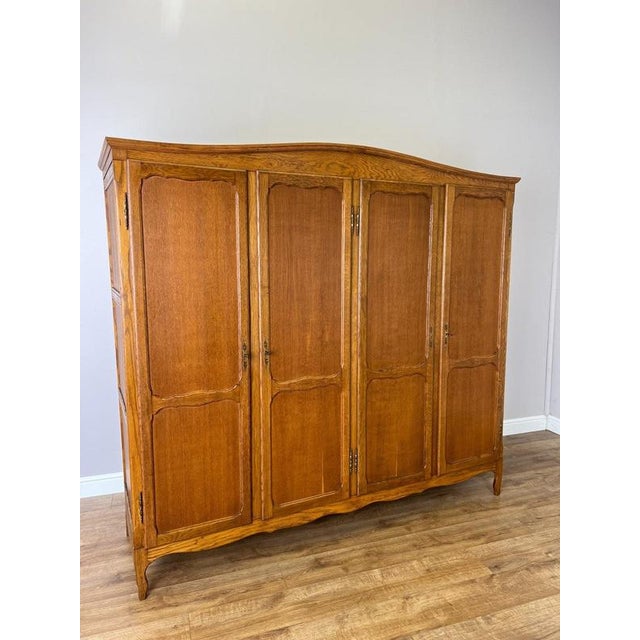 A substantial Vintage French Louis wardrobe in oak, featuring four tall panelled doors, a gently shaped cornice, curved...