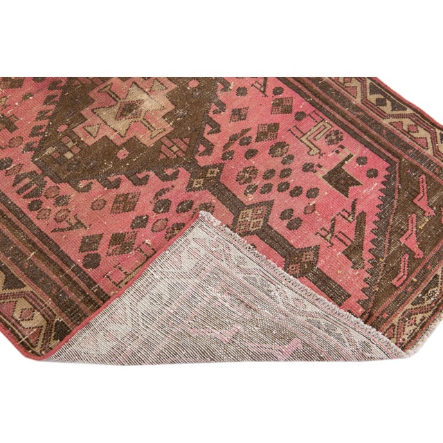 Beautiful vintage Persian distressed hand-knotted wool rug with a pink color field. This piece has a beige frame and brown...