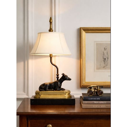 A sculptural vintage table lamp featuring a sleek bronze-tone greyhound or whippet reclining atop a stepped gilt plinth,...