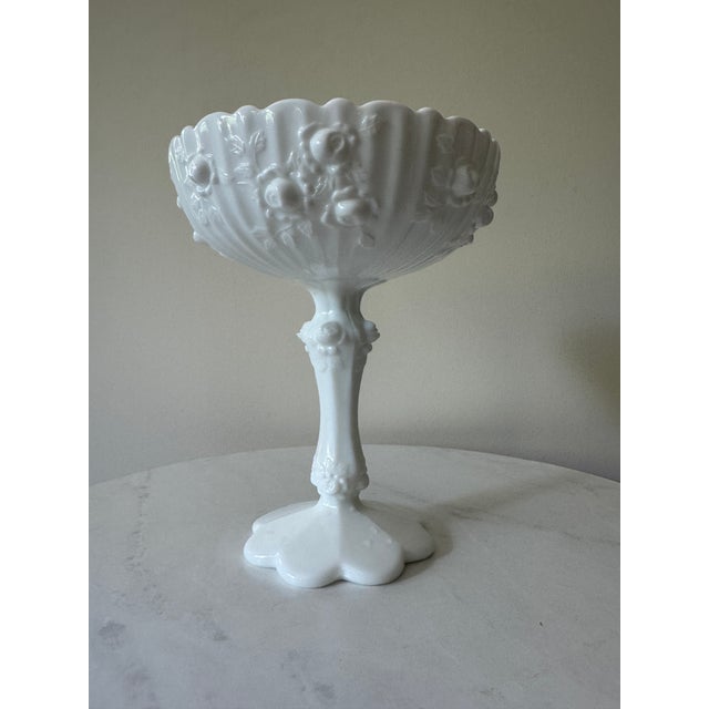 A lovely vintage milk glass compote with beautiful embossed detail, circa 1950s–60s. The wide scalloped bowl features...