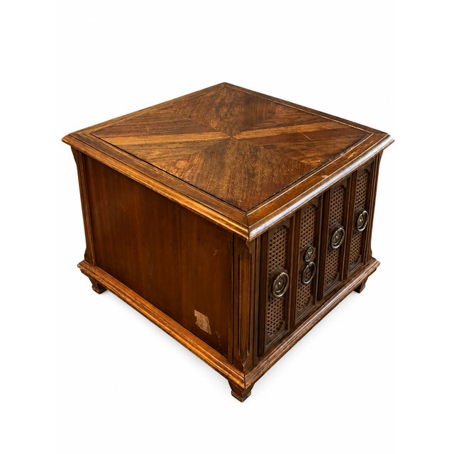 A distinctive vintage cabinet end table featuring a warm brown finish, a geometric figured top, and four decorative cane-...