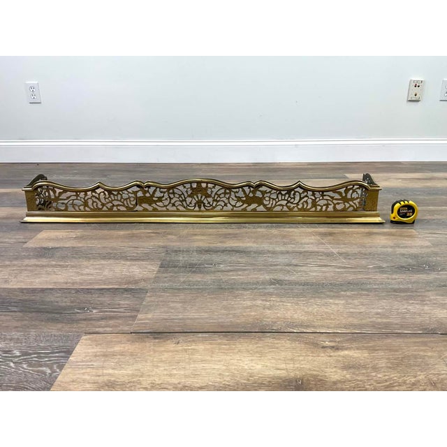 A beautifully detailed vintage brass fireplace fender featuring a graceful scalloped crest rail and finely pierced...