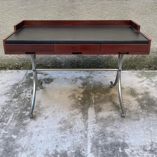 Small desk with three drawers, wooden frame and chromed and curved tubular metal supports. The desk has a slight defect on...