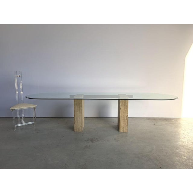 Beautiful trestle shaped travertine and brass dining table with a large oval beveled glass top. The table was made by...