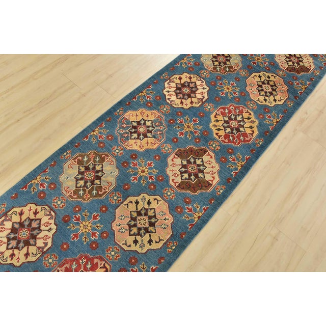 A tribal Caucasian Kazak runner hand-knotted with an all-wool pile on a cotton foundation. This oriental rug features rows...