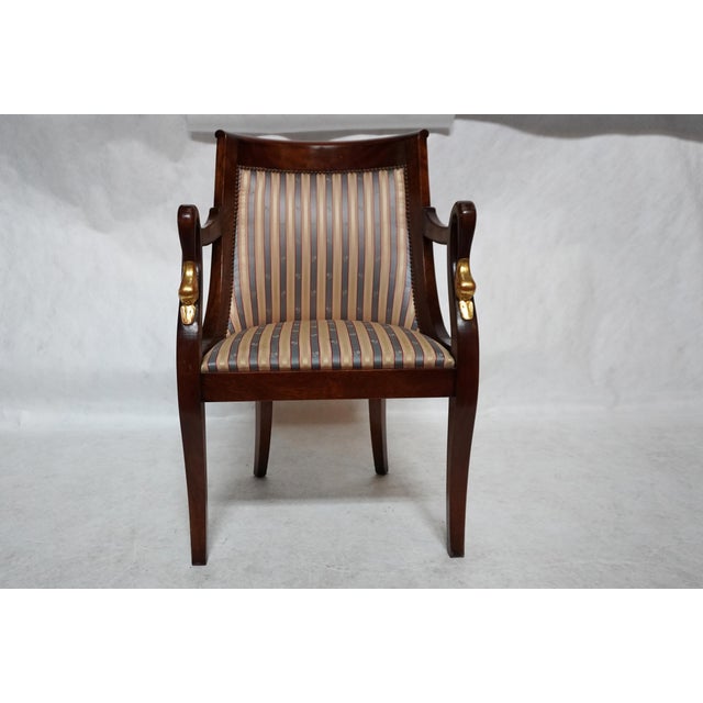Empire-style armchair with an upholstered barrel back. The chair showcases beautifully carved, gold-painted dolphin arm...