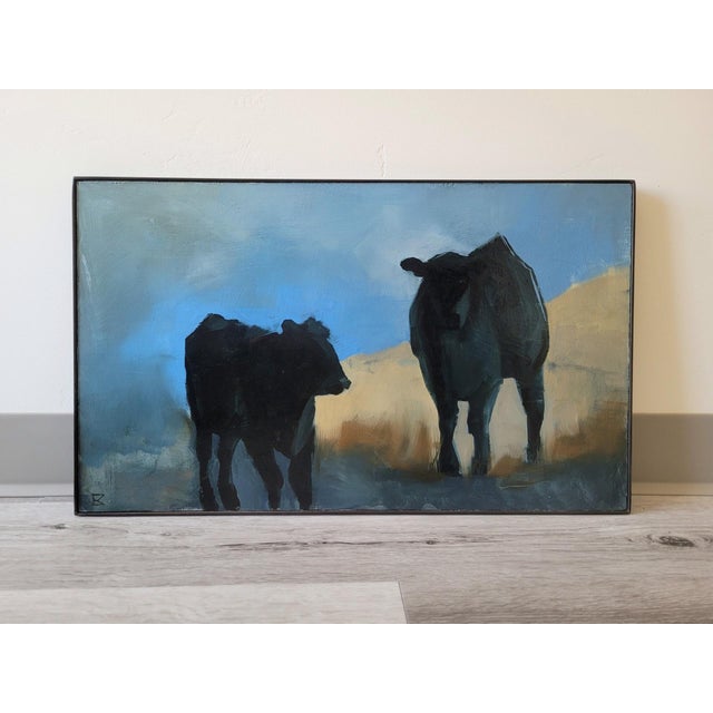 In "Herd Rhythm," two silhouetted cows stand against a soft blue backdrop, evoking a sense of tranquility and connection...