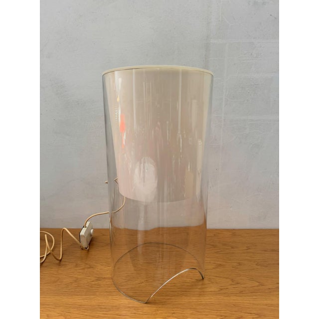 A clear glass cylinder open at the base, with a conical internal diffuser in ivory-colored glass and an exposed bulb on a...