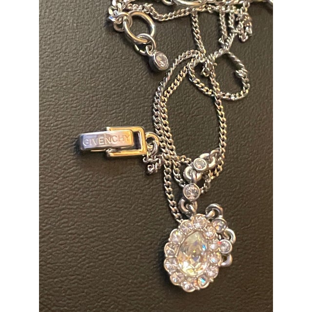 This elegant Givenchy necklace showcases a striking pear-cut crystal pendant framed by a luminous halo of pavé-set round...