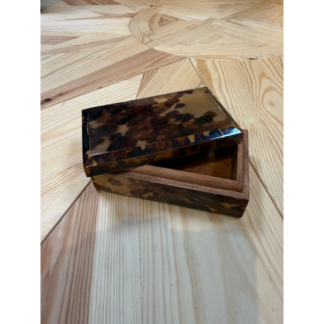 A classic rectangular box finished in a rich faux tortoiseshell lacquer, showcasing a mottled pattern of amber, honey, and...