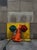 This oil on panel artwork depicts a vibrant orange piece of fabric draped over a yellow fire hydrant, contrasting against...