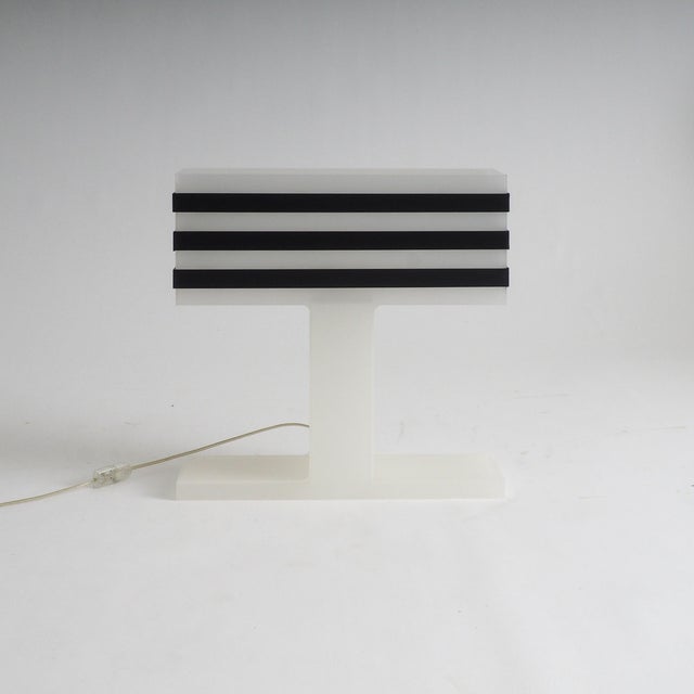 This modernist table lamp features a distinctive geometric silhouette crafted from frosted and black acrylic glass. Its...