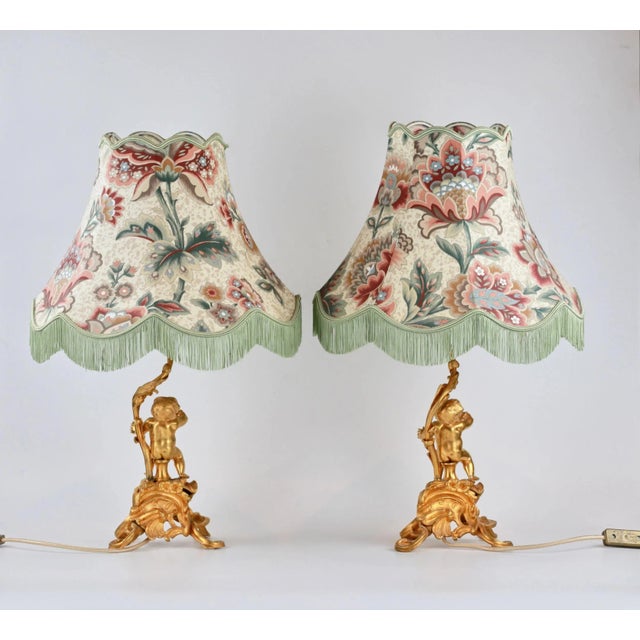 Pair of table lamps "Putti", made of gilded bronze, depicting Putti playing and a stem-shaped plant shoot. Electrified....