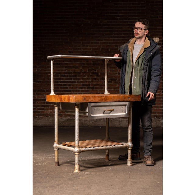 Compact industrial prep station built around a thick, solid butcher block top mounted to a pipe-form steel frame. The...