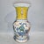This striking porcelain vase features a vibrant yellow ground adorned with intricate blue and white floral motifs on the...