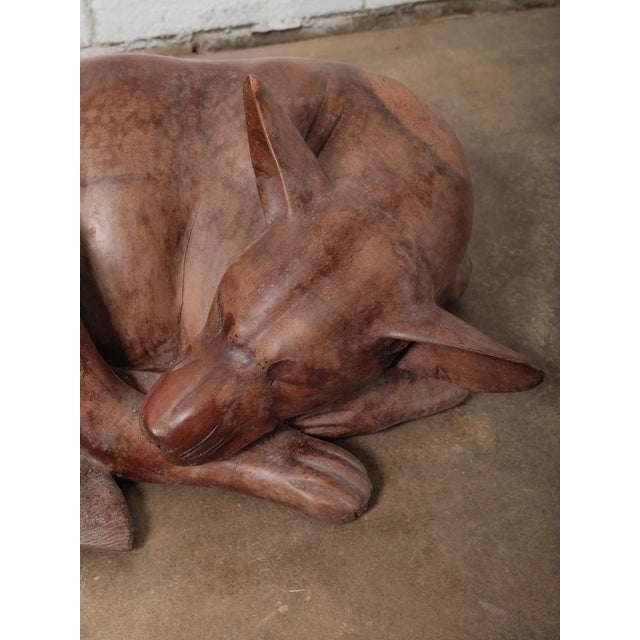 A beautifully sculpted hand-carved wooden figure depicting a sleeping dog, rendered in a tightly curled resting pose. The...