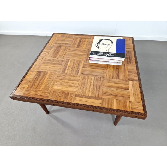 This amazing square coffee table has Wengé sides and a center of parquet shaped wooden strips and teak feet. it just...