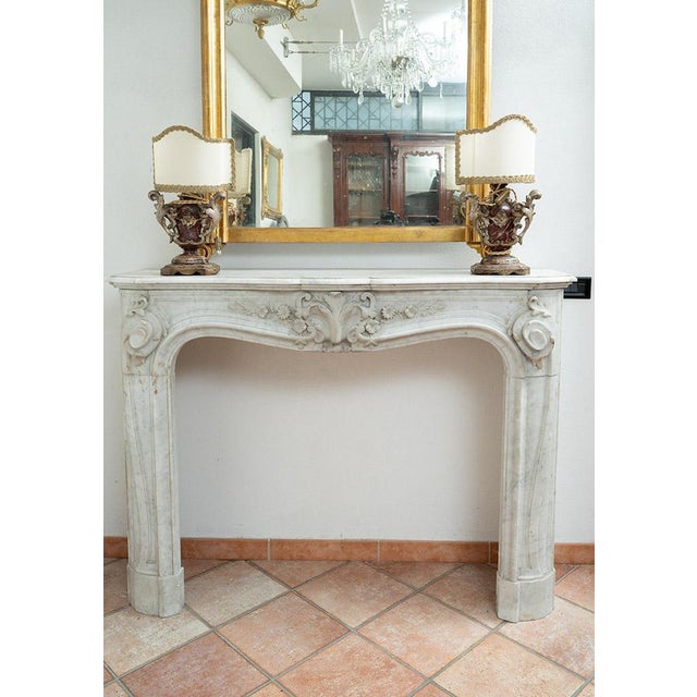 Antique Louis XV-style fireplace in white Carrara marble dating from the early 19th century. The lintel is slightly arched...