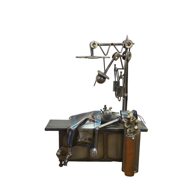Detailed scrap-metal sculpture features a whimsical surgical scene crafted entirely from upcycled industrial hardware. On...