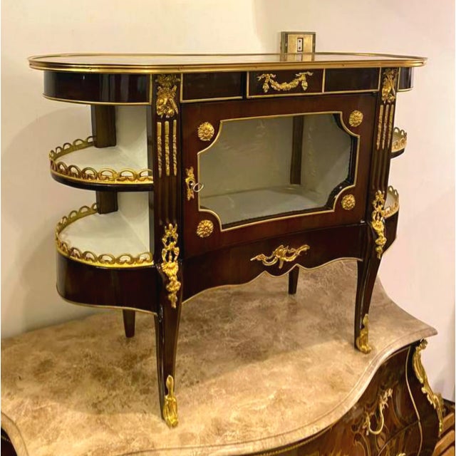 Exquisite French Louis XV-style display cabinet featuring a richly polished dark mahogany finish, ornate gilt bronze...
