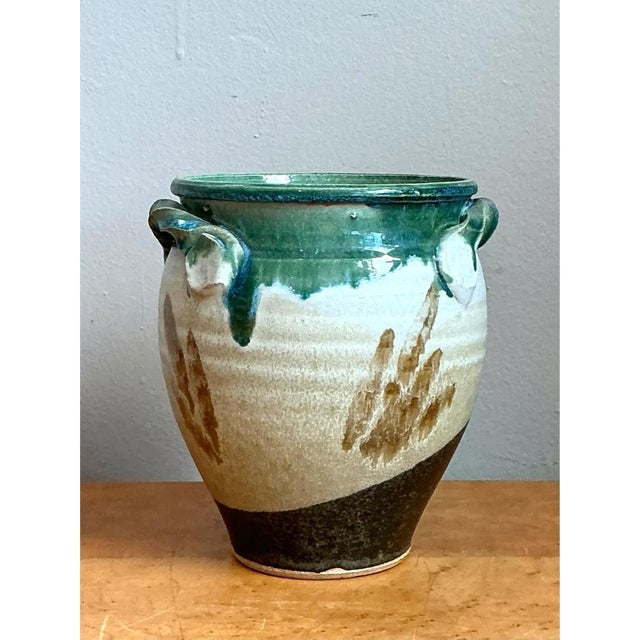 This pottery vase presents a rounded, urn-like silhouette, its body curving gently outward from a narrower base to a...