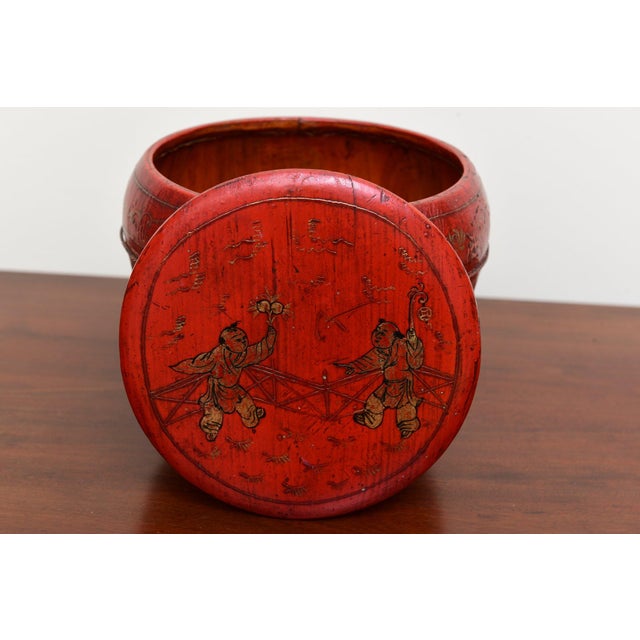 A small antique Chinese red lacquered covered box with a rounded, bulbous form, two painted figures at play amid floral...
